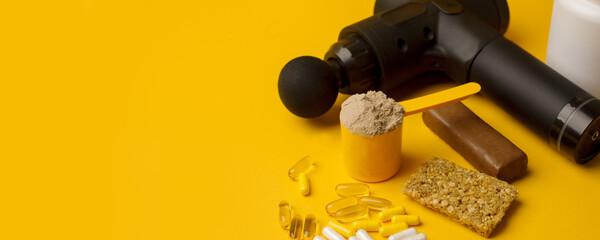 Therapeutic percussive massage gun, fit meal, pills, sport energy bar, protein on yellow background - concept of modern sport activity and diet, health lifestyle routine, wellness, healthcare