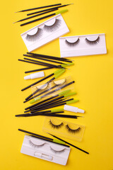 Flat lay composition with false eyelashes, cosmetic products and tools on trendy bright yellow background, concept of lashmakers work place, beauty industry, salon, minimal style