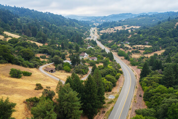 Fototapeta premium Rural highway meanders through hilly, forested landscape with scattered houses and serene surroundings