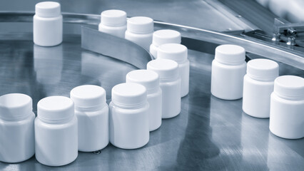 Row of white plastic containers with lids for medicines or vitamins or active dietary supplements on conveyor belt of pharmaceutical factory