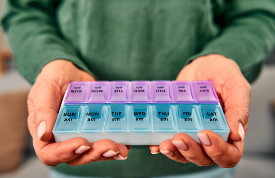 The elderly woman organized her medications for the week ensuring she takes the right dosage each day.The cropped image shows a close-up of elderly women’s hands holding a purple-blue pill box.
