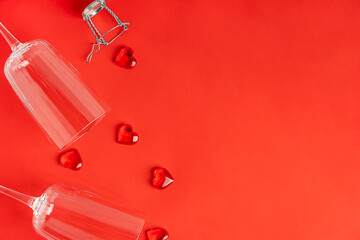 Top view of two empty transparent wine glasses or flute for champagne on bright red background with festive heart shaped holiday decor for greeting on celebration of valentines day or romantic dinner
