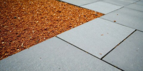 Fototapeta premium Grey paving stones meet reddish-brown granular ground cover in an outdoor setting