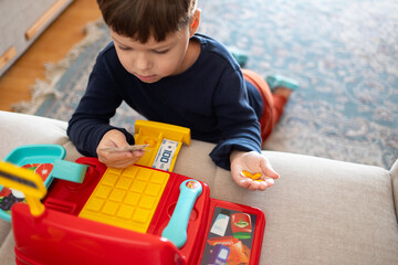 A boy is counting toy money while playing with a toy cash register.