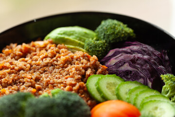 Healthy vegetarian bowl with buckwheat, avocado, broccoli, red cabbage, cucumber, and tomato.