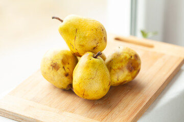 Ripe yellow pears stacked on a wooden cutting board, ready for use in a recipe.  Natural light illuminates the fruit, highlighting their texture and color.