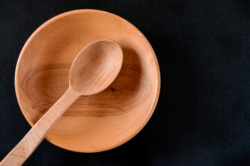Brown wooden spoon in wooden plate on black table
