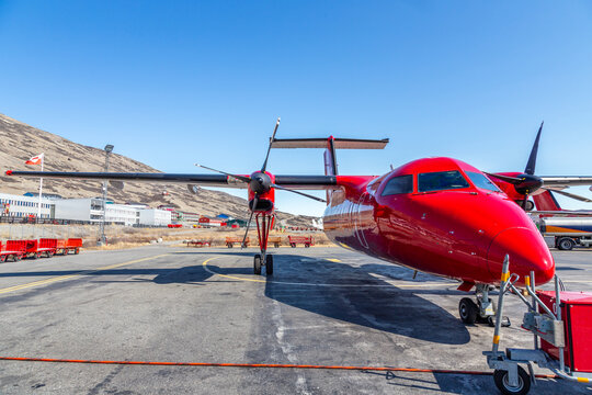 Red propeller plane parked after landing at Kangerlussuaq airport with greenlandic settlement in the background, Greenland