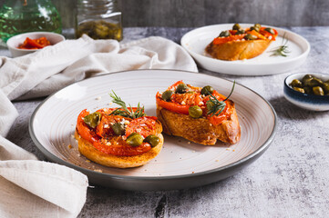 Appetizing bruschetta with dried tomatoes and pickled capers on a plate on the table