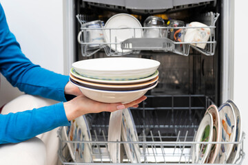 Close-up of female takes of clean dish out of dishwasher machine	