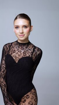 Caucasian model turns and poses in black lace outfit. Snake print body stocking at grey studio backdrop. Vertical video.