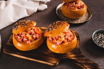 Baked buns stuffed with sausage, tomatoes and cheese on a board on a table