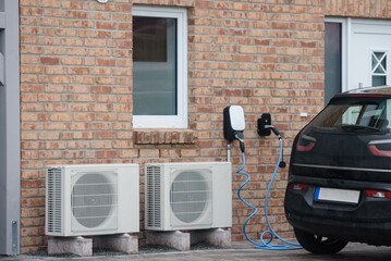 Sustainable living EV charging and heat pumps. Modern home equipped with energy-efficient solutions, including two heat pump units and an electric vehicle (EV) charging station. 
