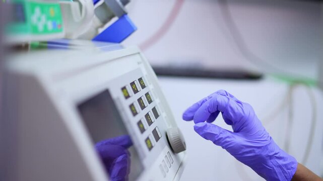 Female hand in blue latex glove turns the handle and presses keys on the medical machine. Preparing the equipment for usage at neurosurgery. Side view close up.