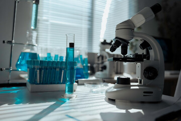 Modern microscope standing on table with test tubes and flasks containing blue liquid in laboratory