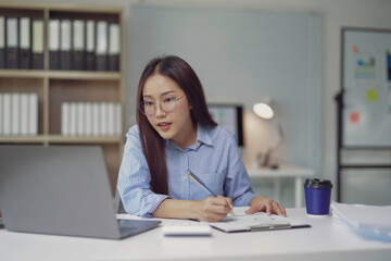 Young Asian businesswoman working at home office using laptop and taking notes