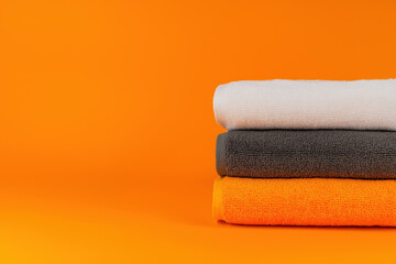 Soft towels stacked neatly against a vibrant orange background in a minimalist setting