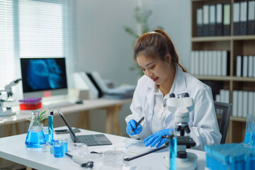 Scientist taking notes in laboratory with blue chemical liquids