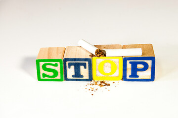 broken cigarette on wood blocks spelling stop with pieces of tobacco on white background