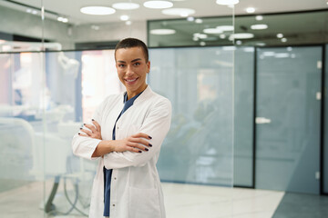 Caucasian female dentist in her dental clinic wearing a white coat, confidently standing with arms...