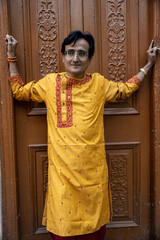 An indian man wearing an indian traditional bengali red dhoti and orange kurta posing outdoor fr a...