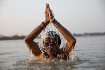 An Indian man taking a holy dip in the river ganges during early morning. he is chest deep...