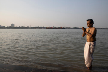 An Indian man taking a holy dip in the river ganges during early morning. he is chest deep...