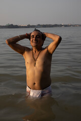 An Indian man taking a holy dip in the river ganges during early morning. he is chest deep...