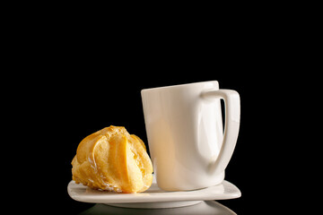 Ceramic cup with eclairs on a saucer, close-up, isolated on a black background.