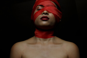 a fashion portrait of a female model wrapped in a red ribbon