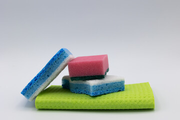 View of three colorful kitchen sponges stacked on a light green towel on a light background