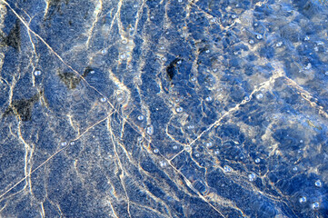 A thin layer of water with ripples on dark marble fountain tiles, illuminated by sunlight. Texture in full screen.