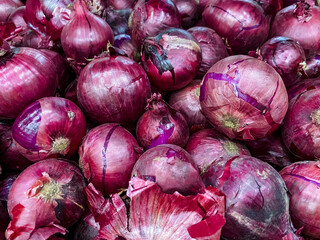 Vibrant red onions, celebrated for their deep and rich color as well as bold flavor, are beautifully stacked on an aged rustic wooden table, ready for diverse culinary uses in any kitchen