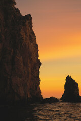 Silhouettes of rocks and birds in the sea, on sunset background. Vertical image