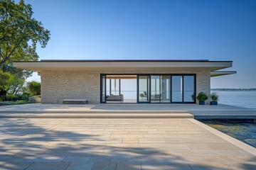 A peaceful waterfront villa with a flat roof, textured stone walls, and expansive sliding glass doors leading to a terrace