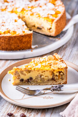 A piece of homemade apple pie with roasted almonds on white wooden background