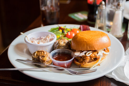 Traditional Irish pub pulled pork burger. Grilled pulled pork burger on a plate with potatoes and salad