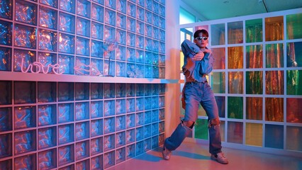 Obraz premium Asian performer with sun glasses moving freestyle dance while looking at camera at nightclub. Happy street dancer dancing and show footstep with colorful bright neon light or led light. Regalement.