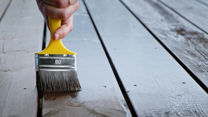 Close-up of a brush painting wood floor in brown color. Wood plank impregnation. Finish oil coating of board. Second layer of oiling. Manual construction work in a gazebo. Natural building materials
