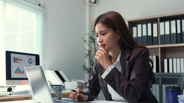 Young businesswoman feeling stressed and tired while working on laptop and reading documents at office desk, experiencing burnout and frustration from work overload