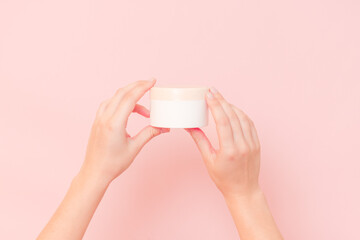 Round jar of cosmetic cream in hand on pink background. Cosmetics beauty mockup for product branding