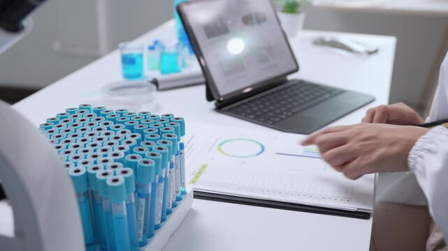 Medical researcher analyzing data on digital tablet, documenting findings with handwritten notes while standing near test tubes rack in modern laboratory setting