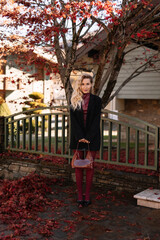 Autumn portrait of a blonde woman in fashionable burgundy clothes walking on the street against the background of a country house outdoors. Selective focus
