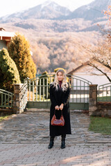 Autumn portrait of a blonde woman in fashionable burgundy clothes walking on the street against the background of a country house outdoors. Selective focus