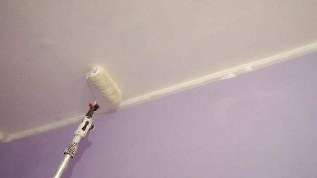 Roller with extension pole applies white paint to ceiling. Interior home improvement. painting services. 