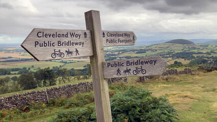 A wooden directional signpost for The Cleveland Way and public bridleway stands in a panoramic...