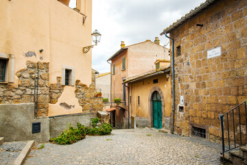 The charming Via del Corso in Tuscania, Italy, showcases a picturesque scene of old buildings with weathered facades and cobblestone paving, creating a timeless atmosphere in this historic town