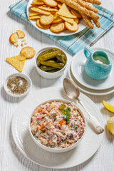 salmon dip with caper, red onion, fresh dill and sour cream in white bowl on white wooden table with crackers, tortilla chips and grissini, vertical view, cose-up