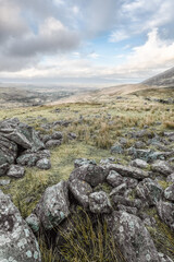 A remote daytime landscape with rugged rocks and hills under dynamic clouds.