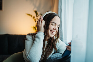 Young caucasian woman listening to music and singing by the window	